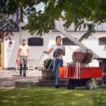 Husqvarna Rider 112iC Batteridriven Åkgräsklippare med ett släp lastas med stolar utanför ett hus